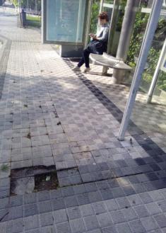 Baldosas levantadas en la acera y parada del autobús